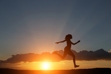 silhouette of a girl running on the hillock right in the beautiful sunset and sea
