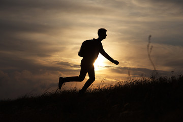 Man runs directly on a hill against a beautiful sunset