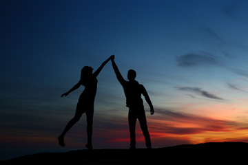 silhouette guy and girl on a beautiful sunset holding hands