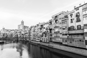 Fototapeta na wymiar Onyar river crossing the downtown of Girona with bell tower of gothic Cathedral of Saint Mary in background. Gerona, Costa Brava, Catalonia, Spain. Monochrome image: black and white.