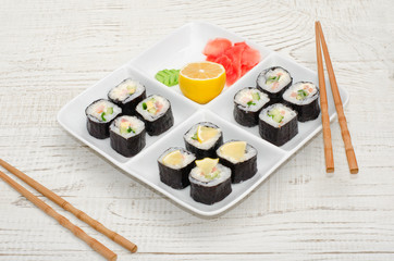 Square plate with a set of rolls on a wooden table. Chopsticks, ginger, lemon. Side view