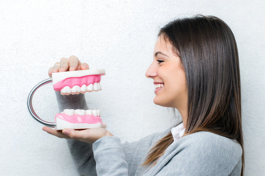 Side view of girl holding oversize teeth prosthesis.