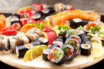 Japanese cuisine. Sushi set on a round wooden board over black concrete background.
