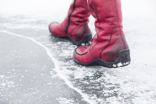 Woman walking on the lake ice surface in winter day.  Red winter boots on legs. Active lifestyle at nature.