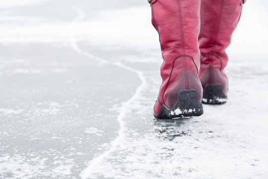Woman walking on the lake ice surface in winter day.  Red winter boots on legs. Active lifestyle at nature.