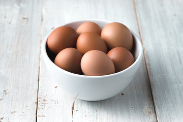 Chicken eggs  in the ceramic bowl on the white wooden table
