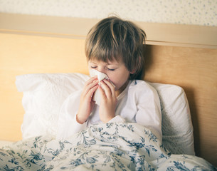 Unhappy ill kid lying in bed and blowing his nose  © Tatiana Murr