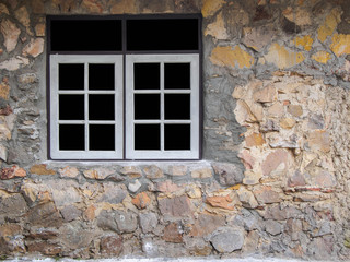White window frame on the wall of a house made of stone.
