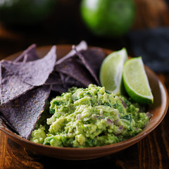 colorful blue corn tortilla chips with fresh mexican guacamole and lime wedges