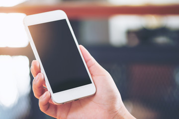 Mockup image of hands holding white mobile phone with blank black screen on vintage wooden room