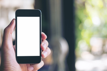 Mockup image of hand holding black mobile phone with blank white screen in loft cafe and green nature