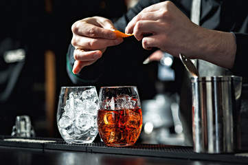 Closeup of bartender hands pouring alcoholic drink into a jigger to prepare a cocktail, with red...