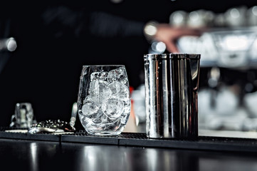Closeup of bartender hands pouring alcoholic drink into a jigger to prepare a cocktail, with red...