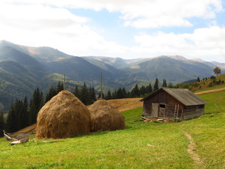 Old wooden hut and haystacks on  background of  beautiful mountain landscape and clouds.