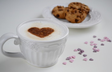 Cappuccino with heart pattern of cinnamon and cookies on the white table