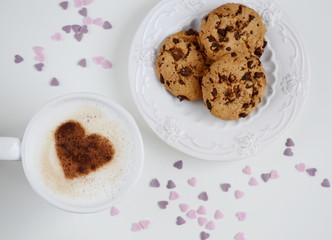 Cappuccino with heart pattern of cinnamon and cookies on the white table