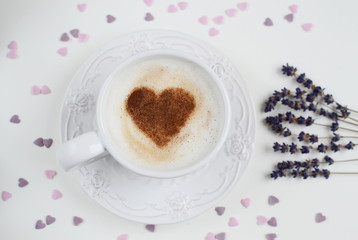 Cappuccino with heart pattern of cinnamon and flowers composition on the white table