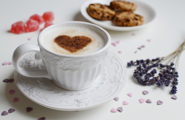 Cappuccino with heart pattern of cinnamon and flowers composition on the white table