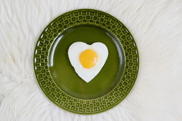 Tasty fried egg in the shape of a heart served on a green plate