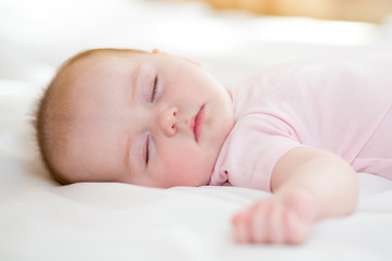 Sweet baby infant lying on a bed while sleeping in a bright room