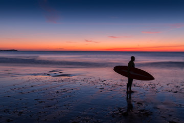 Fototapeta na wymiar Silhouette of surfer on beach at sunset holding surfboard