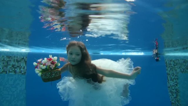 girl in short, white dresses wearing poses underwater in swimming pool