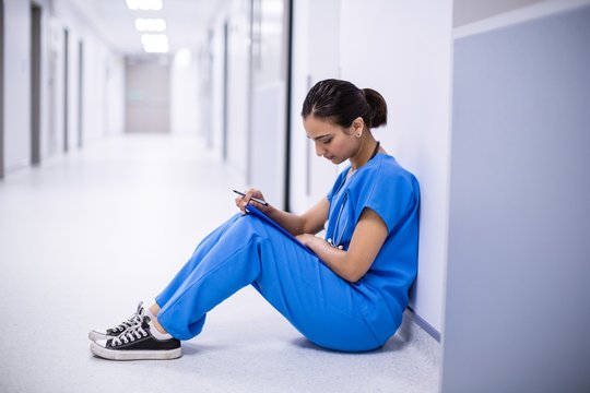 Female Doctor Reading Reports In Corridor