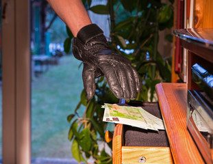 ein Dieb stiehlt aus einer offenen Möbelschublade mehrere Geldscheine