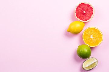 Several kinds of whole and cut citrus on a pink background