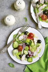 Vegetable salad with chicken and black olives on a white plate.