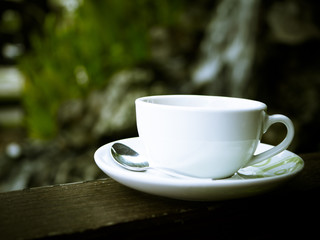 White coffee cup on wooden bench and green bokeh background