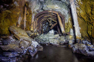 The tunnel of an old abandoned mine with rusty remnants of trolleys