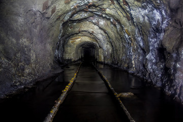 Flooded tunnel of an old abandoned coal mine with rusty remnants of railroad 