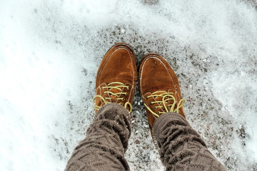 Female feet in shoes on the snowy pavement.