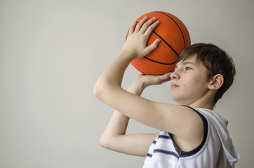 Teenager boy in a white shirt with a ball for basketball on a light background
