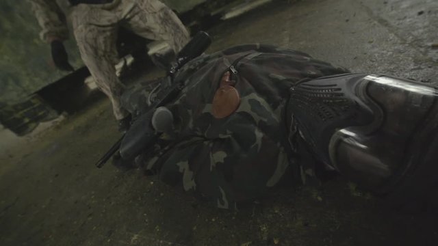 Paintball player in protective uniform jamping down near dead body of the enemy lying on the floor in a mask and camouflage with a gun. Violance and war concept.
