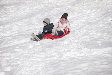 Fototapeta na wymiar Brother and sister on toboggan on snow covered hill