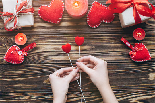 Female holding two love hearts on wooden background with candles and gifts on Valentine day. Romantic atmosphere.