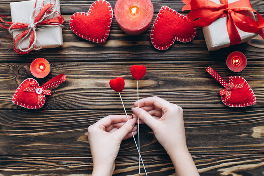Female holding two love hearts on wooden background with candles and gifts on Valentine day. Romantic atmosphere.
