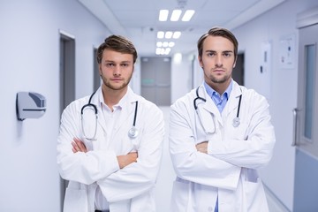 Portrait of doctors standing with arms crossed in corridor