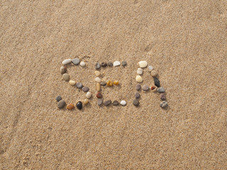 Fototapeta na wymiar word sea written with stones and shells on the beach by the ocean