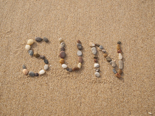 Fototapeta na wymiar word sun written with stones and shells on the beach by the ocean