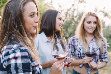 Three young female friends drinking wine in vineyard at sunset