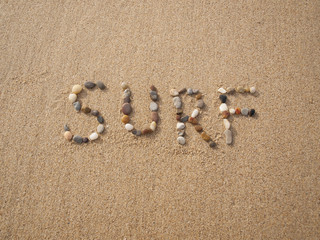 word surf written with stones and shells on the beach by the ocean