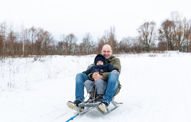 Young man with the little boy sitting on sledge in snow
