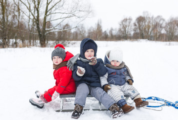 Fototapeta na wymiar Three children sit on the sledge in winter day.