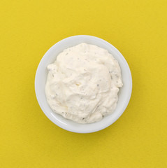 Top view of a small bowl of French onion dip on a yellow tablecloth.