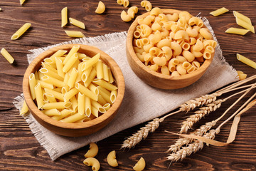 Raw pasta penne  and elbow macaroni in a wooden bowls on the tab