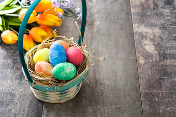 Easter eggs in a basket and tulips on wooden background

