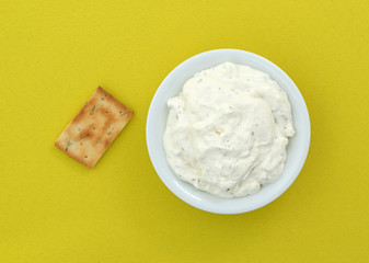 Seasoned rosemary and olive oil crackers with a small bowl of French onion dip atop a yellow tablecloth.